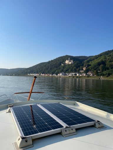 Sonnenkollektoren auf einem Boot mit Blick auf eine Burg und hügelige Landschaft.