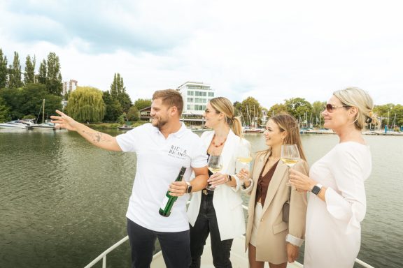 Vier Personen stehen auf einem Boot und genießen den Ausblick auf das Wasser.