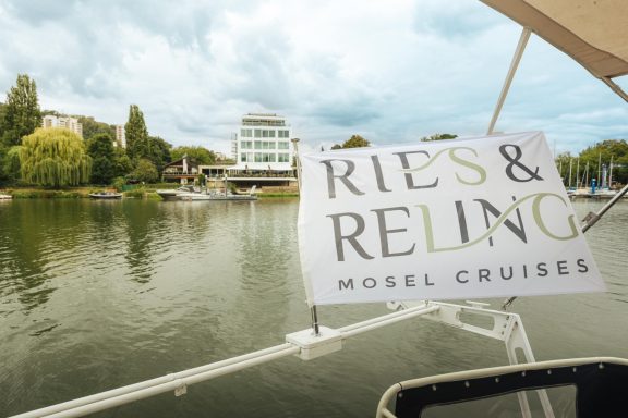 Schild mit der Aufschrift "Ries & Reiling Mosel Cruises" am Wasser.