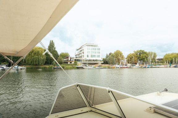 Blick vom Boot auf ein ruhiges Gewässer mit einem modernen Gebäude im Hintergrund.